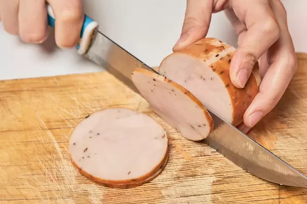 Woman slicing tasty smoked chicken fillet