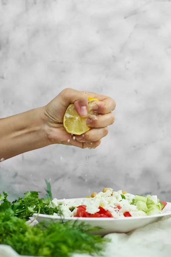 Woman squeezing lemon in a plate with a healthy vegetable salad