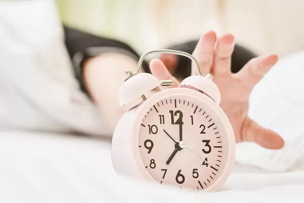Woman stretching hand to ringing alarm to turn it off.