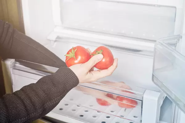 Woman taking fresh tomatoes from the salad crisper drawers of refrigerator