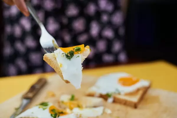 Woman taking fried egg slice with a fork and eating