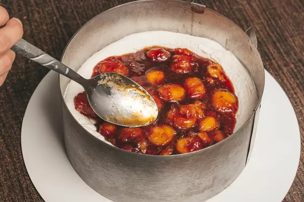 Woman using a spoon to smooth out the strawberry-banana layer in the cake