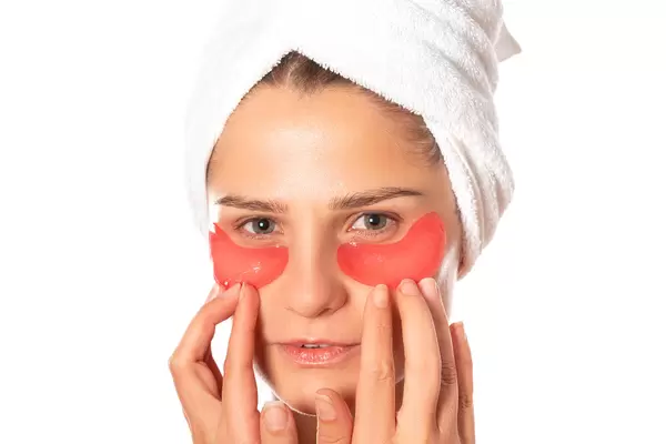 Woman with applied sheet patches under her eyes on white background