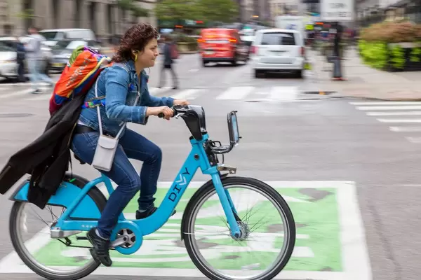 Woman with backpack and jacket attached to it rides a bicycle from the bike sharing service Divvy in the streets of Chicago