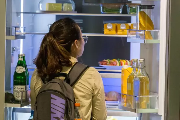 Woman with backpack stands in front of a big fridge and looks at healthy foods