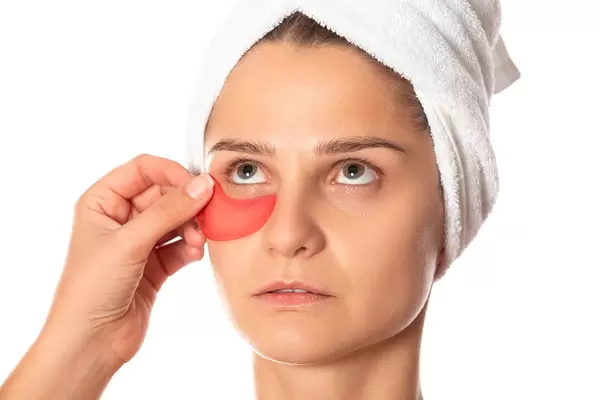 Woman with white towel on head, wears collagen patches under eyes