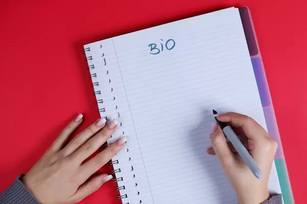 Woman writing Bio text on notebook, red background