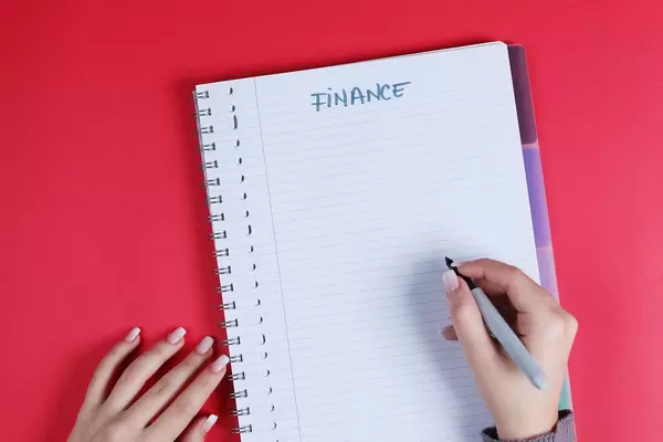 Woman writing Finance text on notebook, red background