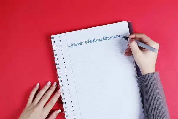 Woman writing Lieber Weihnachtsmann text on notebook, red background