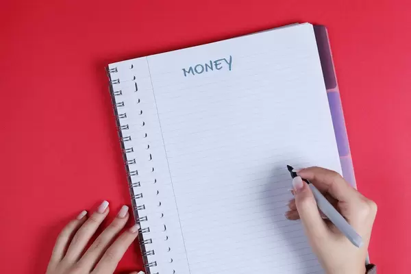 Woman writing Money text on notebook, red background