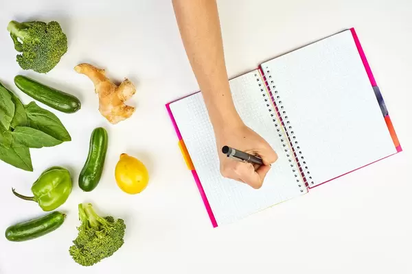 Woman writing on a notepad. Weight-loss planning with fresh vegetables