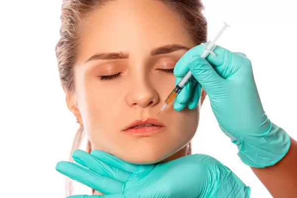 Woman's face and doctor's hands in gloves make an injection above the lip