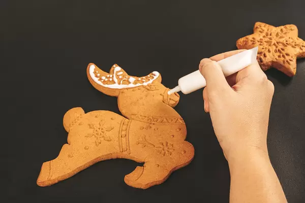 Woman's hand decorates a deer gingerbread, preparing for christmas