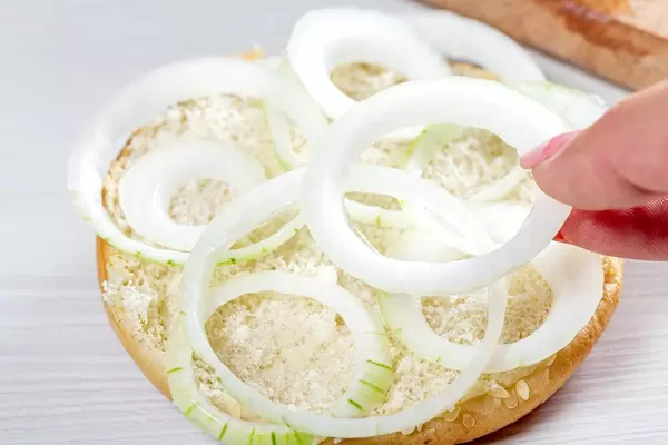 Woman's hand puts onion rings on half of hamburger bun (Flip 2019)