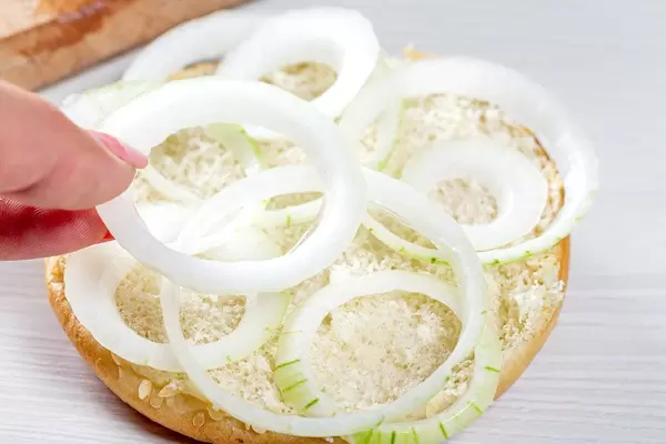 Woman's hand puts onion rings on half of hamburger bun