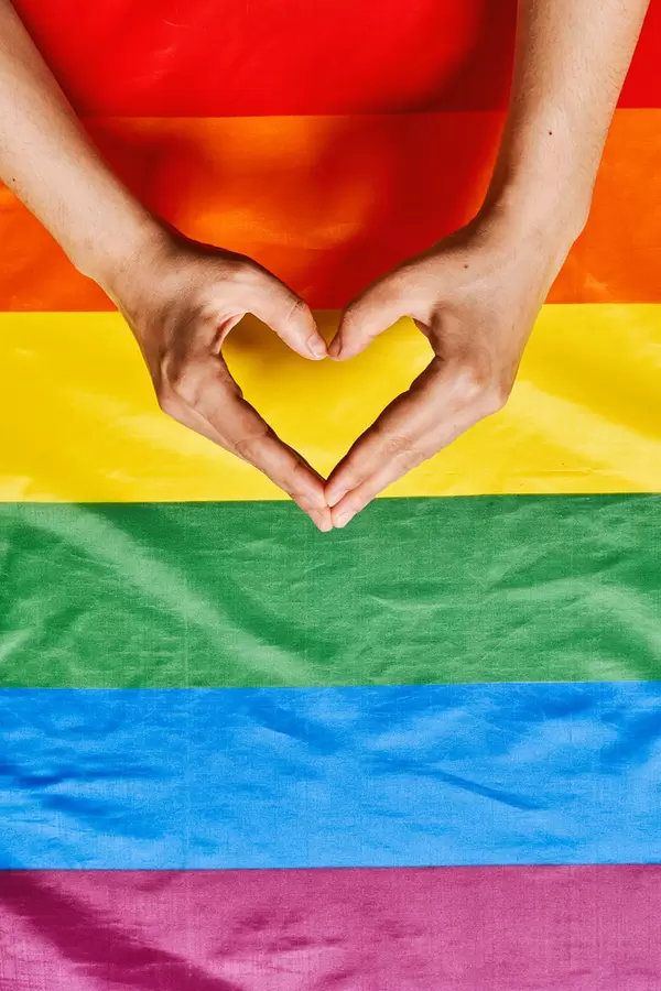 Womans hands making heart shape over the lgbtq rainbow flag background