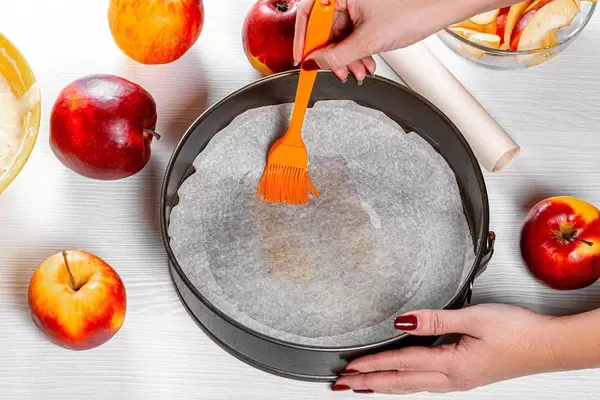 Women grease a baking sheet with butter using a pastry brush