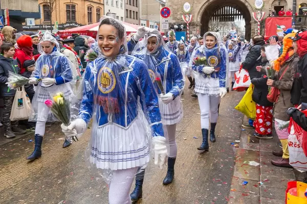 Women parade in traditional blue-white costumes and rain ponchos and hold roses in their hands as the Rose Monday parade starts at Severinsburgtor in Cologne