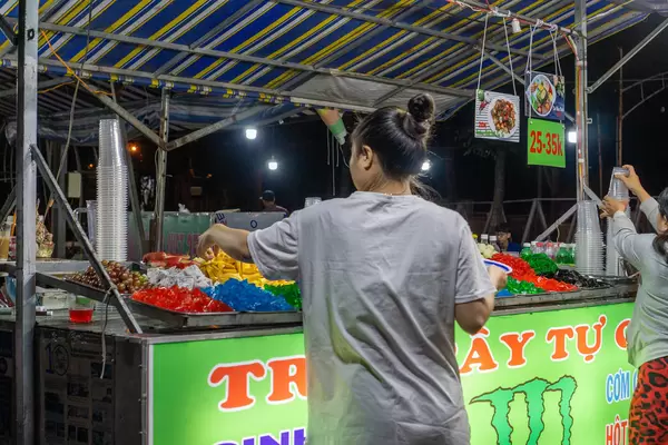 Women picking different Fruits and Jelly to make their own Fruit Bowl at a Street Food Vendor at a Night Market in Can Tho, Vietnam