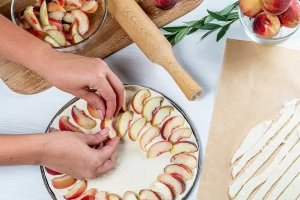 Women's hands lay pieces of peaches on the dough. Cooking peach pie (Flip 2019)