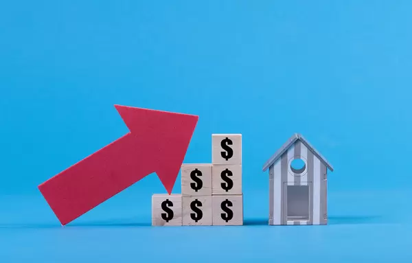 Wooden blocks with Dollar symbol and up arrow with miniature house on blue background