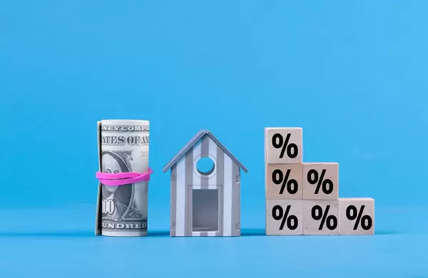 Wooden blocks with percentage sign with money roll and miniature house on blue background