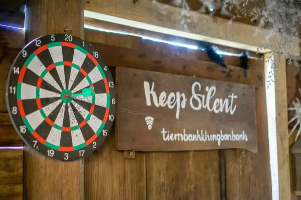 Wooden Board with Words Keep Silent and WiFi Password next to a Dart Board