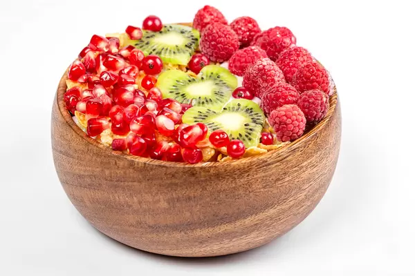 Wooden bowl with cornflakes, yogurt, pomegranate, kiwi and raspberries