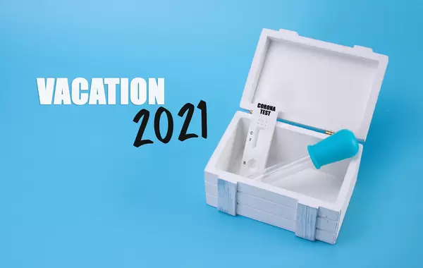 Wooden box with Coronavirus test and Vacation 2021 text on blue background