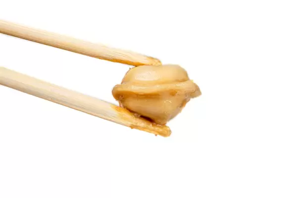 Wooden chopsticks holding a dumpling on a white background