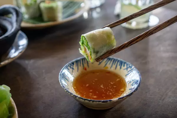 Wooden Chopsticks with Fresh Vietnamese Spring Roll over Fish Sauce with Chili as Dip in an authentic Vietnamese Restaurant