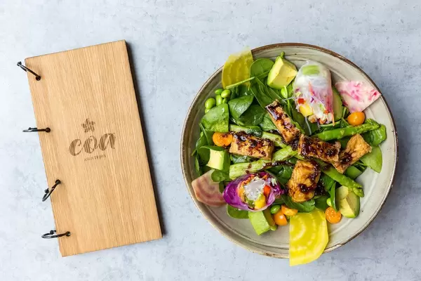 Wooden menu and vegan tofu dish of the coa Wok & Bowl restaurant with tofu, baby spinach, beetroot, avocado, summer rolls, mint and raspberry-miso-dressing