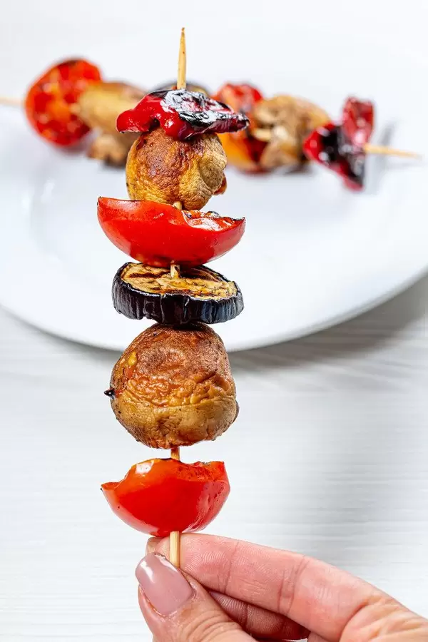 Wooden skewer with mushrooms, tomatoes, eggplant and sweet pepper in hand (Flip 2019)