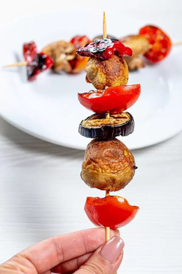 Wooden skewer with mushrooms, tomatoes, eggplant and sweet pepper in hand