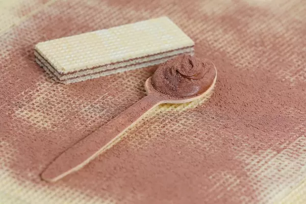 Wooden spoon filled with cocoa and chocolate cream on wafer background (Flip 2019)