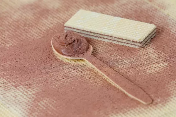 Wooden spoon filled with cocoa and chocolate cream on wafer background