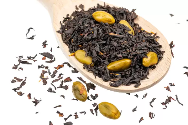 Wooden spoon with dried black tea and green seeds