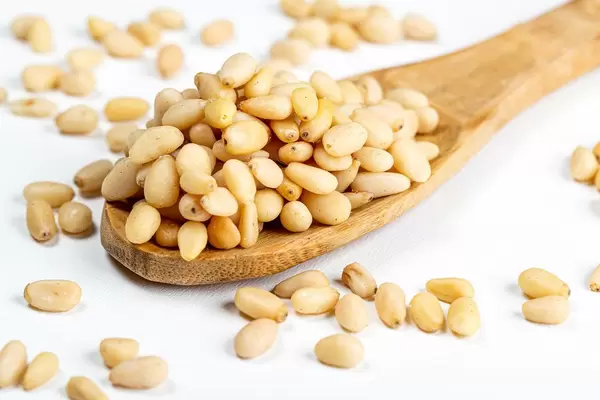 Wooden spoon with pine nuts on a white background