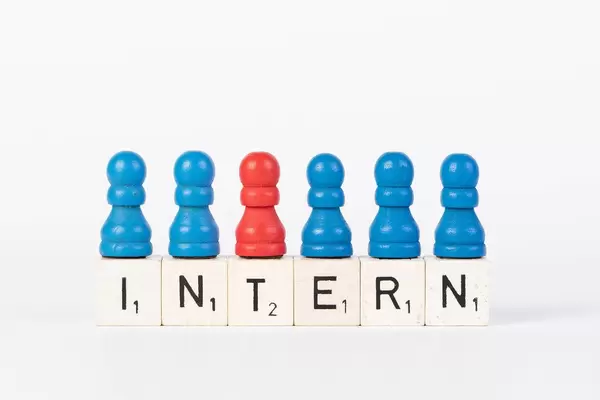 Word Intern written on wooden blocks with pawns in various colors on white background