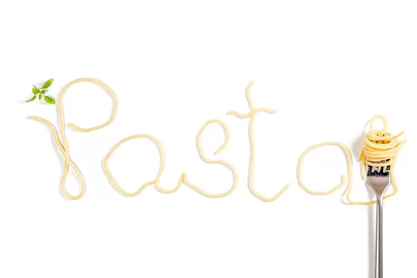 Word pasta made from boiled spaghetti on white background with fork and basil