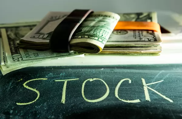 Word STOCK with dollar bills behind