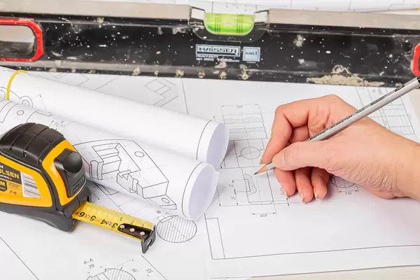 Workspace with drawings, measuring tape, level, and hand with pencil