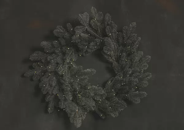 Wreath of branches of a christmas tree with a garland on a dark wall