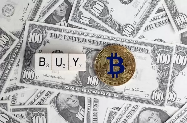 Würfel bilden das Wort Buy neben Bitcoin Münze auf US-Dollar Banknoten