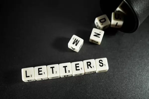 Würfel bilden das Wort "Letters" - Buchstaben - neben herausfallenden Würfeln aus einem dunklen Würfelbecher