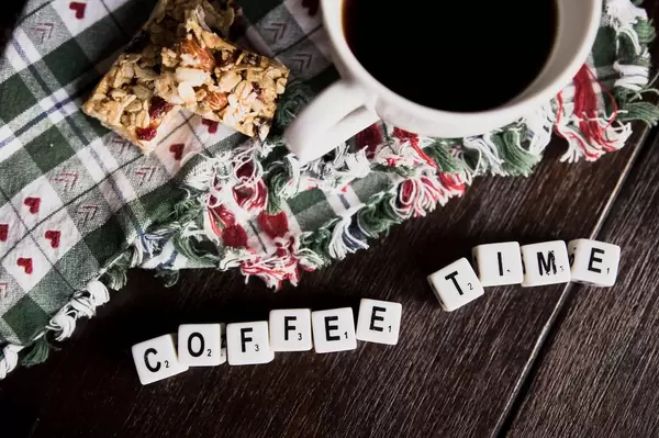 Würfel ergeben den Begriff "Coffee Time" - Kaffeezeit,  neben einer Tasse mit schwarzem Kaffee und einem Müsliriegel