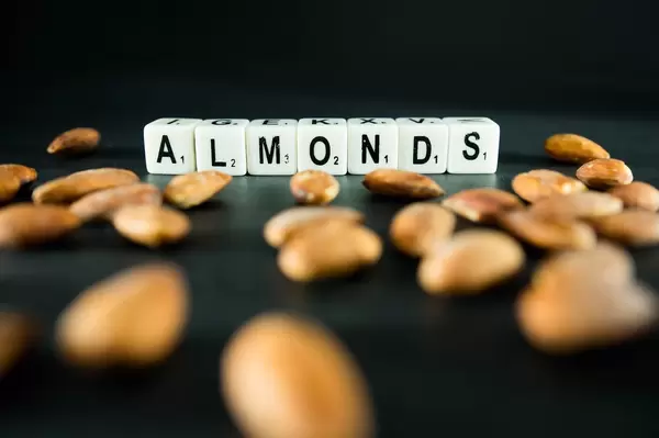 Würfel mit Buchstaben bilden das Wort ALMONDS vor geschälten Mandelkernen
