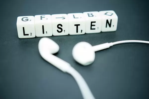 Würfel mit Buchstaben bilden das Wort LISTEN neben weißen Kopfhörern