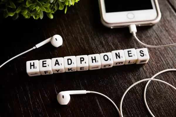 Würfel zeigen das Wort "Headphones" - Kopfhörer, neben einem weißen Iphone auf einem Holztisch