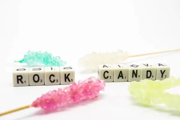 Würfel zeigen das Wort "Rock Candy" - Kandiszucker, umgeben von süßen Zuckerspießen, auf weißem Untergrund